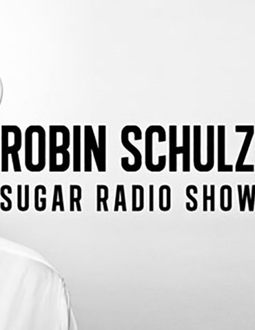 A black and white image of chart hit artist Robin Schulz. He is wearing a shirt and large, white sunglasses. He looks to the right with a neutral expression at the words "Robin Schulz Sugar Radio Show"